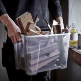 Eine Person hält einen durchsichtigen Plastikbehälter mit Holzwerkzeugen in der Hand, der zum Organisieren und Aufbewahren bereit ist.