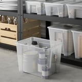 Stauraum mit SAMLA-Boxen in verschiedenen Größen, Reinigungsmitteln in den größten, Regalen mit kleineren Gegenständen, Holzkisten und Tellern.