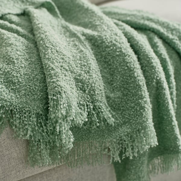 Ein Stapel weicher, grüner, strukturierter Überwürfe aus recyceltem Polyester, die ordentlich drapiert sind.