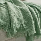 Ein Stapel weicher, grüner, strukturierter Überwürfe aus recyceltem Polyester, die ordentlich drapiert sind.