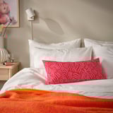 Leuchtend rotes SANDMOTT Kissen auf dem Bett, rechteckig, gemustert, weißer Hintergrund.