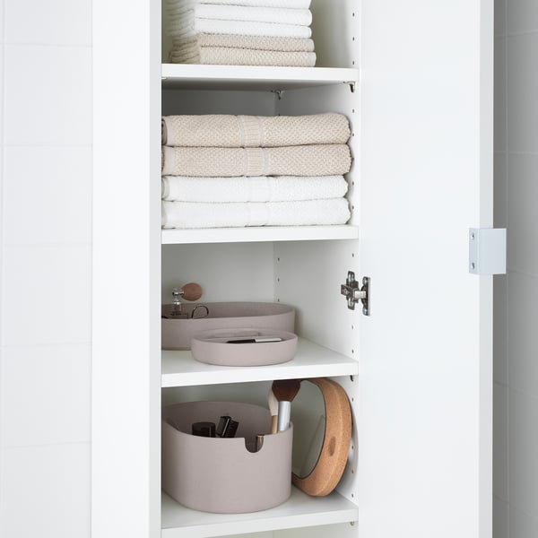 Weißer Schrank mit gefalteten Handtüchern und runden rosa Aufbewahrungsboxen mit Fächern und Spiegel im Inneren.