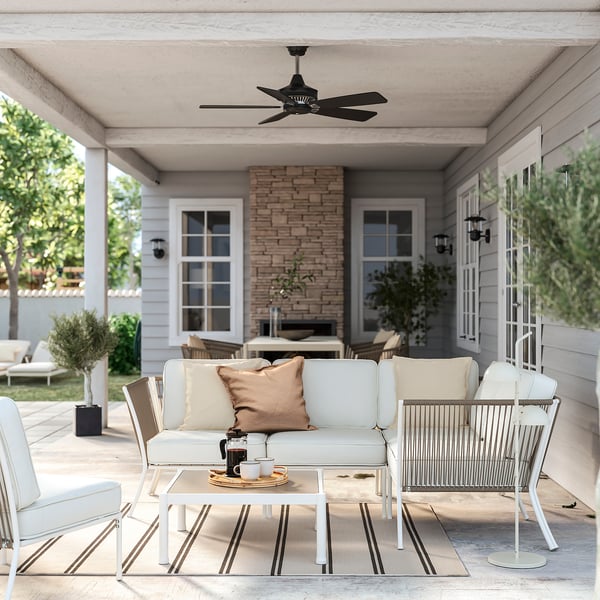 Kompaktes Terrassenset mit cremefarbenen Kissen, Glastisch, Wandleuchten und Deckenventilator.