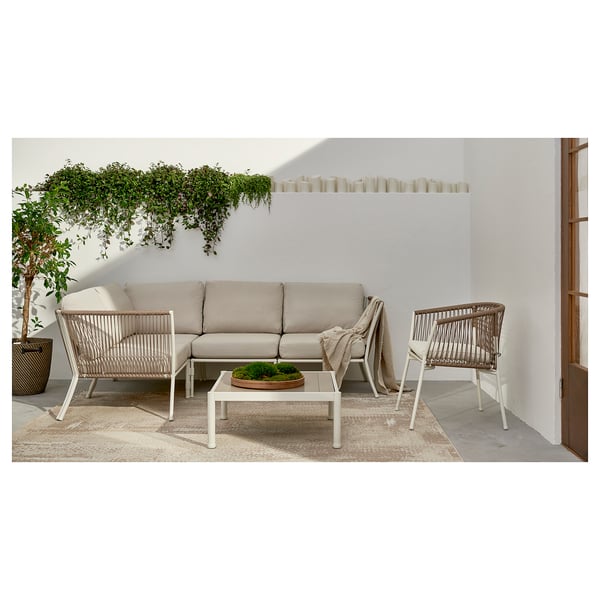 Moderne Sitzgarnitur für den Außenbereich mit beigen Kissen. Verwobene Stühle und Sofa, umgeben von viel Grün.
