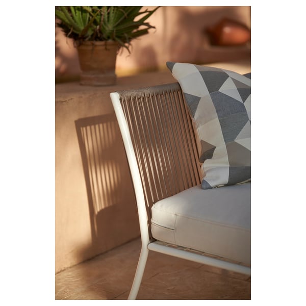 Moderner Outdoor-Stuhl mit weißem Kissen und geometrischem Kissen. Rückenlehne aus geflochtenem Seil und Holzboden.
