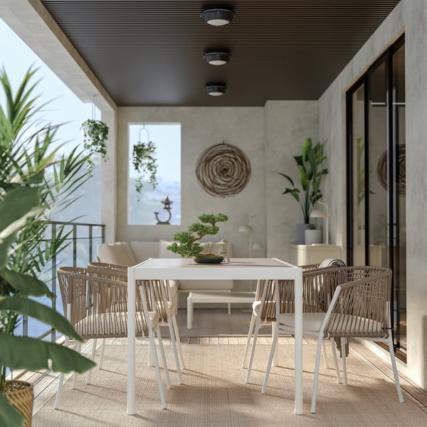 Modernes Esszimmer im Freien mit weißem Metalltisch und geflochtenen Stühlen auf einer Terrasse mit Betonwänden und hängenden Pflanzen.