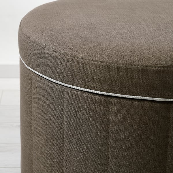 Nahaufnahme einer gut gearbeiteten, runden Ottomane mit getuftetem Design und grauen Paspeln, die hochwertige Polster und Nähte zeigt.