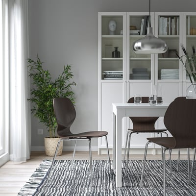 Minimalistischer Essbereich mit zwei SIGTRYGG-Stühlen, verchromt, in der Nähe eines weißen Tisches. Bücherregale mit Dekor, Pflanzen und gemustertem Teppich.