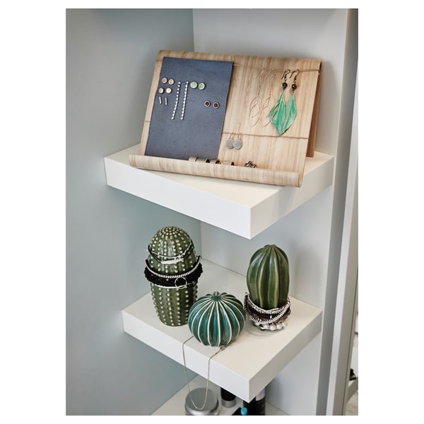 Weiße Regale mit grünen Keramikkakteen. Ein Kaktus hält Silberschmuck. Die Regale stehen an einer hellblauen Wand.