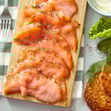 SJÖRAPPORT kalt geräucherter Lachs auf einem Holzbrett mit frischem Dill, Salat, Zwiebeln und Crackern.