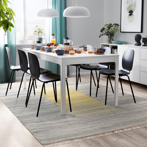Modernes Esszimmer mit weißem Tisch, schwarzen Stühlen, gestreiftem Teppich, Essen und Pendelleuchten.