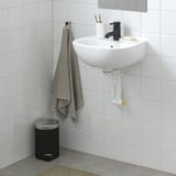 Weißes Wandwaschbecken SKATSJÖN, schwarzer Wasserhahn, tiefe Schüssel, graues Handtuch, schwarzer Müll.