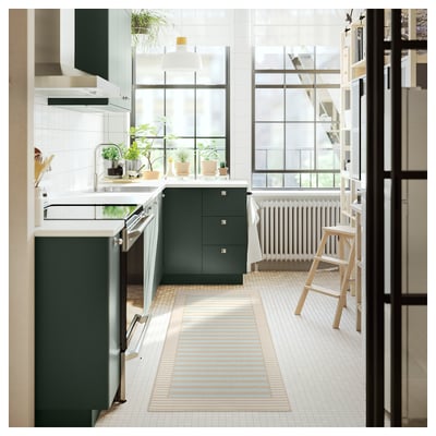 Moderne Küche mit dunkelgrünen Schränken, weißen Fliesen und einem gestreiften beige und blauen Läufer. Große Fenster lassen natürliches Licht herein.