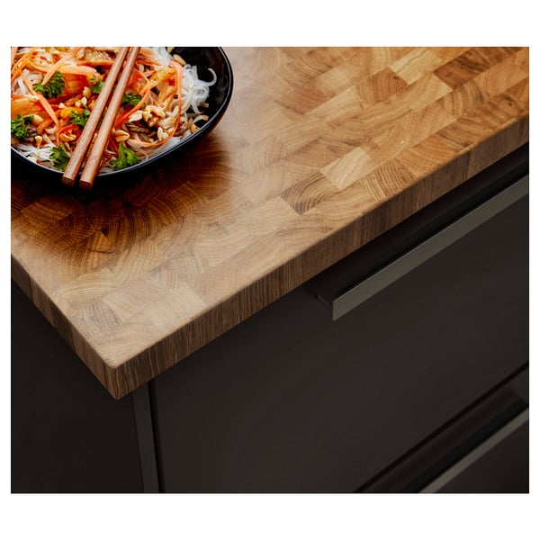 Eine SKOGSÅ-Arbeitsplatte aus Holz mit einer Schüssel mit Essen darauf. Die Arbeitsplatte ist hellbraun mit einer natürlichen Holzmaserung und hat einen dunklen Griff.