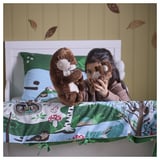 Mädchen umarmt Otter-Plüschtiere auf einem Bett mit Naturmotiven.