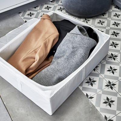 Weißer Aufbewahrungsbehälter mit hellbrauner und grauer Kleidung im Inneren, der für den Einsatz unter dem Bett oder im Kleiderschrank konzipiert ist, mit Belüftung für Frische.