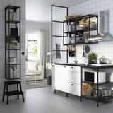 Moderne Küche mit weißen Schränken, schwarzen Regalen, Edelstahlgeräten, Töpfen, Mikrowelle, Wasserkocher, Bild und gefliesten Wänden.