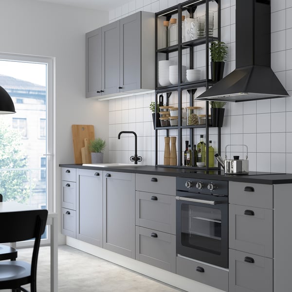 Moderne Küche mit grauen Schränken, schwarzen Armaturen, LED-Leuchten, Glasregalen, Edelstahlgeräten und großem Fenster.