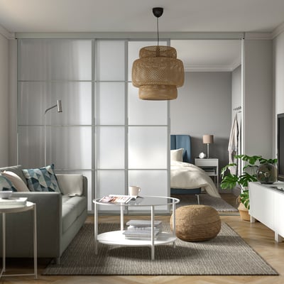 Modernes Studio-Apartment mit grauer SKYTTA-Schiebetür, Kingsize-Bett, grauem Sofa, Couchtisch, Korblampe, Pflanzen, minimalistischem Dekor.