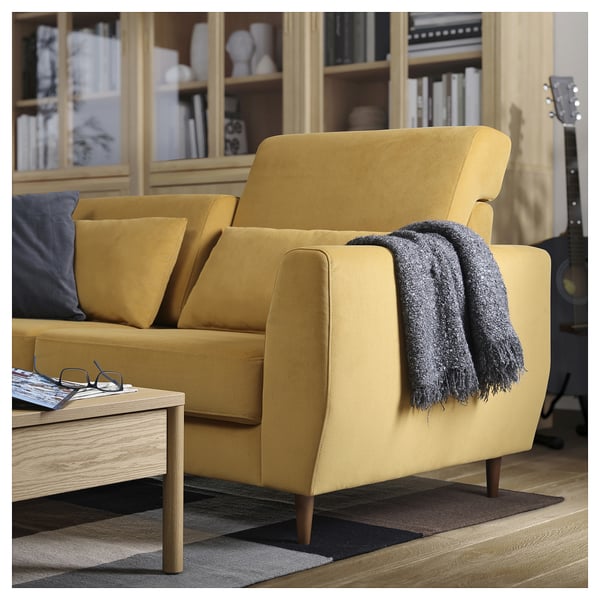 Modernes gelbes Sofa mit Holzbeinen, grauer Decke in gemütlicher Wohnzimmereinrichtung.