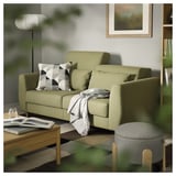 Ein modernes Wohnzimmer mit einem grünen SLATORP-Sofa, weichen Kissen, Büchern und einer kuscheligen Decke.