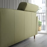 Modernes grünes Sofa mit ausziehbaren Rückenkissen für zusätzlichen Komfort, in der Nähe eines Fensters mit Pflanzen.