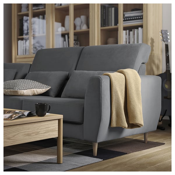 Ein modernes graues SLATORP-Sofa mit einer beigen Decke, einer schwarzen Tasse und Büchern auf einem Holztisch. Das Sofa hat gepolsterte Kissen und Holzbeine.
