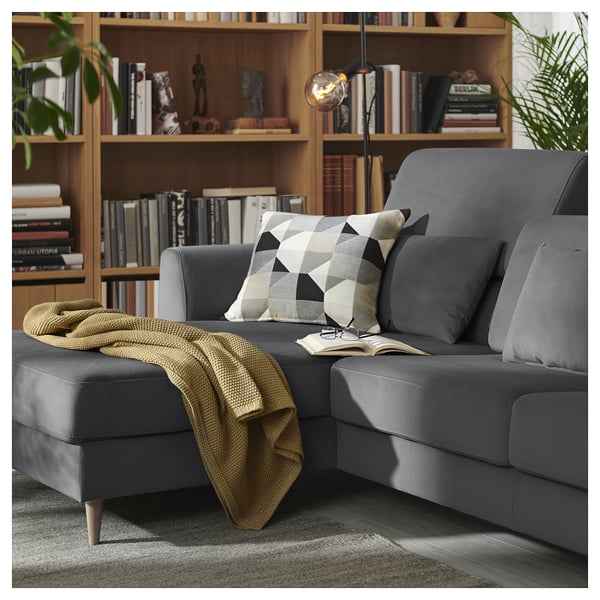 Dunkelgraues L-förmiges Sofa mit Holzbeinen, Kissen, Decke und Bücherregal.