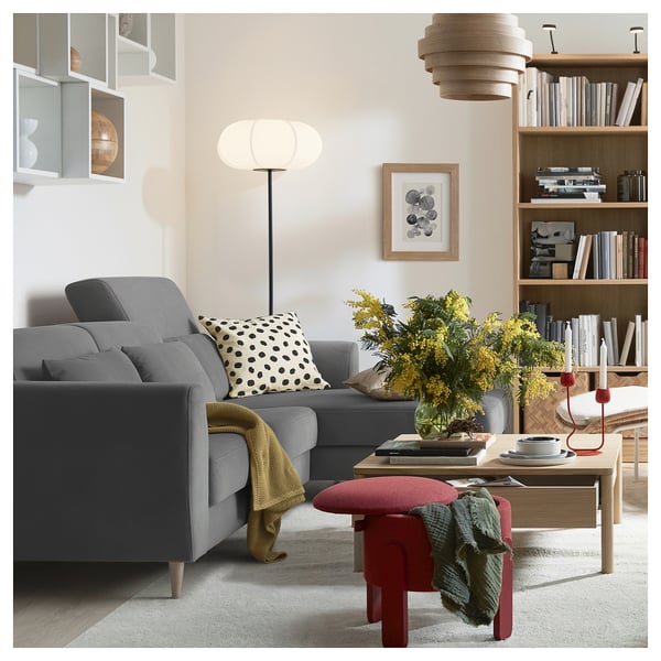 Ein modernes Wohnzimmer mit einem grauen SLATORP-Sofa, einem Couchtisch aus Holz, einem roten Hocker, einem gelben Überwurf und einem Bücherregal mit Büchern und Dekorationsartikeln.