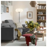 Ein modernes Wohnzimmer mit einem grauen SLATORP-Sofa, einem Couchtisch aus Holz, einem roten Hocker, einem gelben Überwurf und einem Bücherregal mit Büchern und Dekorationsartikeln.