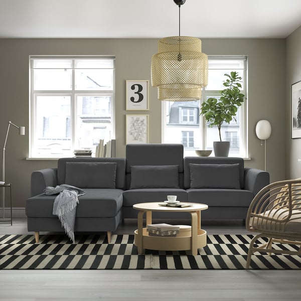 Modernes Wohnzimmer mit grauer SLATORP-Sektion, schwarz-weißem Teppich, Couchtisch aus Holz, Korbstuhl, großen Fenstern und stilvoller Pendelleuchte.