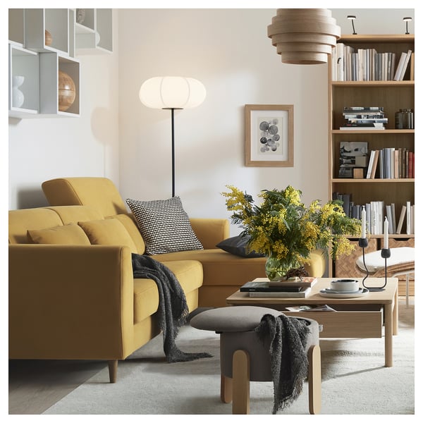 Modernes gelbes Sofa mit verstellbaren Kissen und Holzbeinen, gemütlicher Überwurf, Büchern, Lampe.