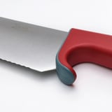 Nahaufnahme eines Küchenmessers aus Edelstahl mit rotem Griff und blaugrünem Kropf, das seine hochwertige Klinge und sein ergonomisches Design zeigt.