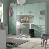 Helles Homeoffice: hellgrüne SMÅSTAD-Einheiten mit weißem Schreibtisch und Stuhl, schwarzem Rucksack, grauer Decke, Naturholzboden, weichem Teppich und Pflanze.