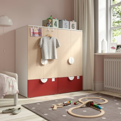 Modernes Kinderzimmer mit SMÅSTAD-Kleiderschrank, grauem T-Shirt, roten Schubladen, Spielzeugeisenbahn, weißem Bett.