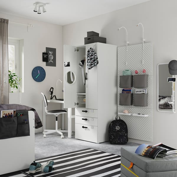 Modernes Jugendschlafzimmer mit weißem SMÅSTAD-Kleiderschrank, gestreiftem Teppich, grauem Stuhl, schwarzem Rucksack, Postern und grauer Bettwäsche.