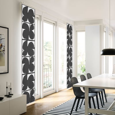 Modernes Wohnzimmer mit hohen schwarz-weißen Vorhängen, Esstisch, schwarzen Stühlen, Kerzenständern und gestreiftem Teppich, der von natürlichem Licht durchflutet wird.