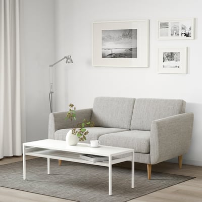 Modernes Wohnzimmer mit grauem SMEDSTORP-Sofa, weißem Tisch, Schwarz-Weiß-Drucken, Vase und Tasse.