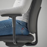 Sitzende Person auf SMÖRKULL-Bürostuhl mit verstellbarer Armlehne.