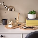 Schreibtisch mit SMÖRLING Tabletts, einem Becher und einer Pflanze. Tabletts bieten Platz für Malutensilien und Seile. Heller und organisierter Arbeitsbereich mit einer Lampe.