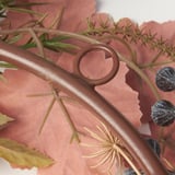 Brauner Kranz mit getrockneten Blumen und dunklen Beeren, aus nächster Nähe, auf rosa Textil.