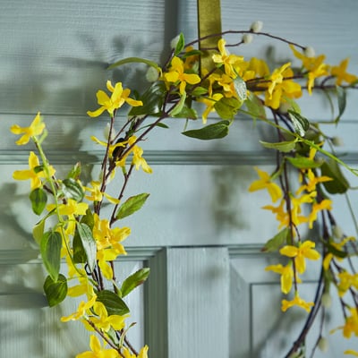 Kreisförmiger gelber Blumenkranz mit grünen Blättern aus recyceltem Kunststoff.
