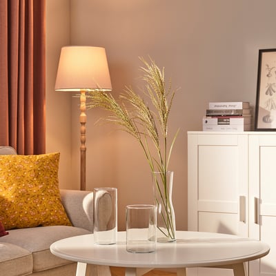Wohnzimmer mit Beigetönen. In der Mitte des Tisches befinden sich Vasen und getrocknete Pflanzen. Couch, Lampe und Bücherregal sind sichtbar.