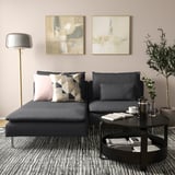 Modernes Wohnzimmer mit einem großen grauen SÖDERHAMN-Sofa, geometrischen Kissen, einem runden Couchtisch, einer Lampe und Gemälden.