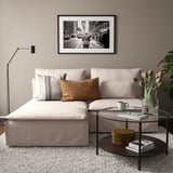 Modernes Wohnzimmer mit beigem Sofa, Chaiselongue, Kissen, Glastisch, Lampe, Kunst. Gemütlich, stilvoll, zeitgemäß.