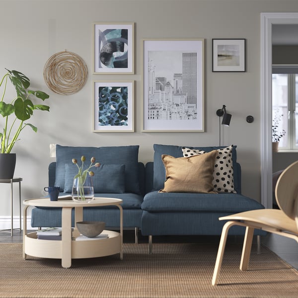Modernes Wohnzimmer: blaues SÖDERHAMN Sofa vor grauer Wand mit abstrakter Kunst. Couchtisch aus Holz, Pflanze und Tageslicht.