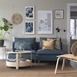 Modernes Wohnzimmer: blaues SÖDERHAMN Sofa vor grauer Wand mit abstrakter Kunst. Couchtisch aus Holz, Pflanze und Tageslicht.