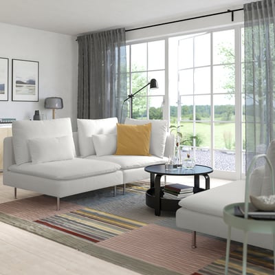 Modernes Wohnzimmer mit weißem SÖDERHAMN-Sofa, gelbem Kissen, gestreiftem Teppich, schwarzem Couchtisch, Lampe und großen Fenstern mit Vorhängen.