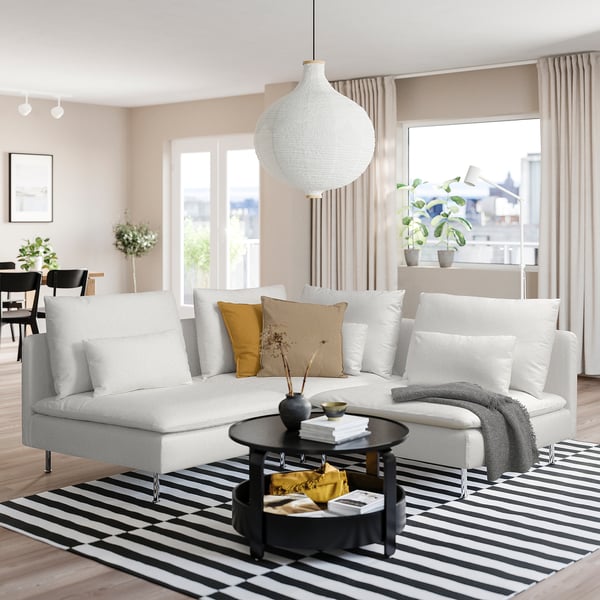 Modernes Wohnzimmer mit SÖDERHAMN-Sofa, Holzboden, gestreiftem Teppich, Couchtisch mit Büchern und großem Fenster mit beigen Vorhängen.