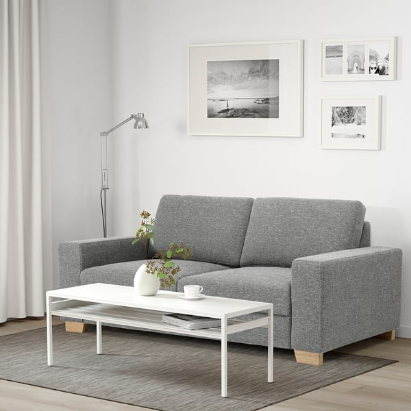 Ein modernes Wohnzimmer mit einem grauen Sofa, einem weißen Tisch und einer Lampe. Wandkunst schmückt helle Wände.